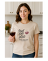 Woman holding a glass of wine wearing a 'Pinot State of Mind' t-shirt in a kitchen.